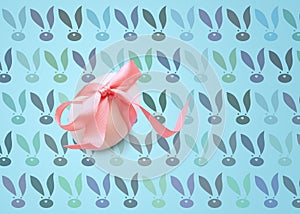 Isolated one easter white egg with pink ribbon on a blue background with a pattern of Bunny rabbit muzzles. Happy Easter holiday