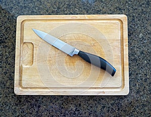 Isolated paring knife on a large wooden cutting board with a granite kitchen counter
