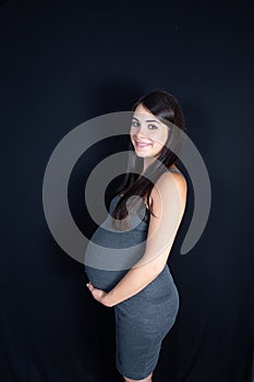 Isolated portrait of beautiful smiling woman in dress waiting for baby in black background