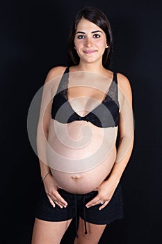 Isolated portrait of beautiful smiling young woman in dress waiting for baby in black background