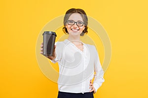 Isolated portrait of confident beautiful young smiling happy business woman offering cup of coffee on yellow background