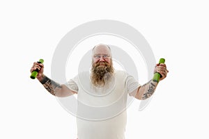 Isolated portrait of an overweigh bearded man with tattooed arms exercising with dumbbells and having serious looking at camera