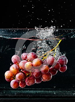 Isolated Red grapes splashing and sinking in water on black background