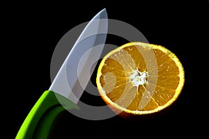 Isolated ripe orange fruit cut in half. exposed inner texture. White porcelain knife blade. Black background. 