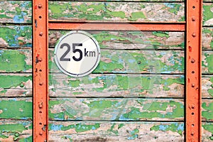 Isolated round metal speed limit 25 km sign on weathered colorful wooden planks with peeling paint on back of agricultural trailer