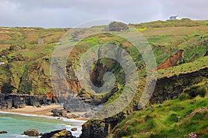 Isolated sandy cove beneath rugged cliff overlooked by a lone white house on the north coast of Cornwall England.