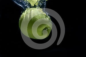 Isolated shot of a green apple submerging into the water in front of a black background