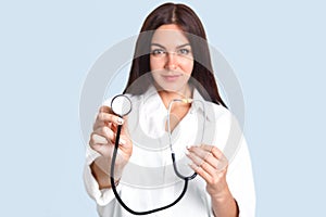Isolated shot of prett confident female doctor advertises her new phonendoscope, ready to examine people, hear lungs and heart, is photo