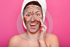 Isolated shot of surprised woman applies mask on face, has happy facial expresion, opens mouth from amezmant, having rest while photo