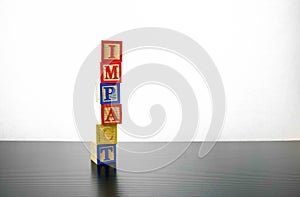 Isolated stacked wooden cubes  for IMPACT with over grey background. Conceptual impact of financial and economic uncertainties