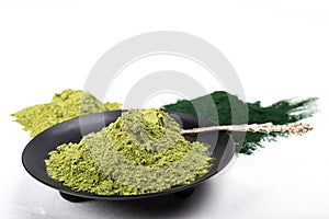 An isolated tablespoon of dried organic wheat grass and spirulina powder, on white rustic background