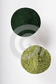 An isolated tablespoon of dried organic wheat grass and spirulina powder, on white rustic background