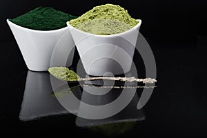 An isolated tablespoon of dried organic wheat grass and spirulina powder, on white rustic background