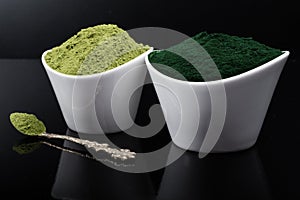 An isolated tablespoon of dried organic wheat grass and spirulina powder, on white rustic background