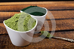 An isolated tablespoon of dried organic wheat grass and spirulina powder, on white rustic background