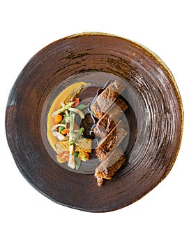 Isolated top view of roasted medium rare wagyu beef served with sour sauce with roasted baby vegetables on stone plate