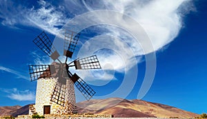 Isolated traditional round spanisch stone windmill Molino de Tefia, dry arid hilly landscape, blue sky white cloud -