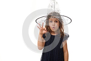 Isolated waist length portrait of pretty little witch girl wearing a wizard hat and dressed in stylish carnival dress, gesturing,