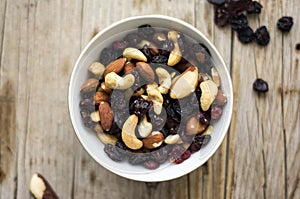 Isolated little white bowl of mixed nuts and dried fruits on the rustic background