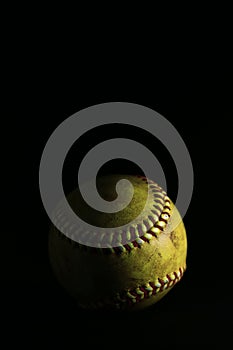 Isolated yellow softball with red seams on a black background.