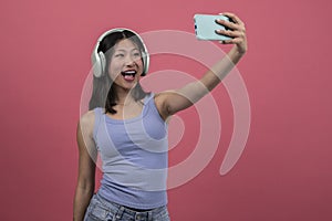 Isolated young female laughing listening to music taking a picture with smartphone. Woman with headphones and phone