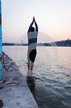 Isolated young man prying the holy ganges river at river bank from flat angle