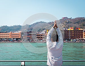 Isolated young man prying the holy ganges river at river bank from flat angle