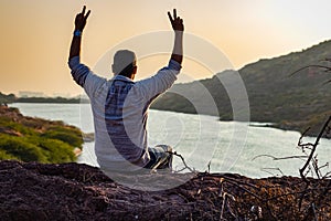 isolated young man sitting at mountain top with lake view from flat angle