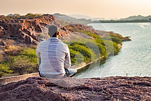 isolated young man sitting at mountain top with lake view from flat angle