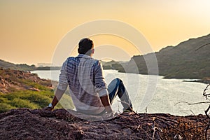 isolated young man sitting at mountain top with lake view from flat angle