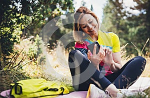 Isolation girl laughing using smartphone technology after training in park. Smile woman relax after exercising sport outdoors