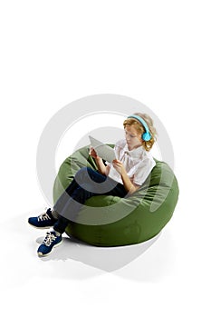 Isometric view. Little boy, child with blonde hair sitting in headphones and looking on tablet against white background