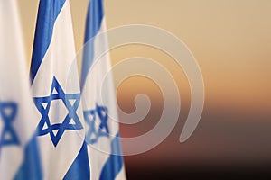 Israel flags with a star of David over cloudy sky background on sunset. Banner with place for text.