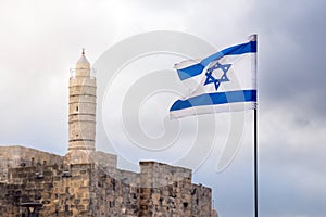 Israeli flag flutters in the wind with a minaret of a mosque on the background in Jerusalem