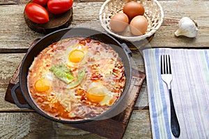 Israeli fried eggs shakshuka with cheese in a frying pan next to a fork and a napkin.