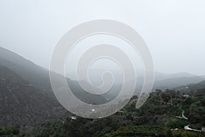 Istan, Spain, Andalusia - A winding road disappears into the fog-covered mountains, evoking a sense of mystery and