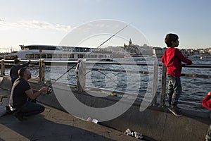 ISTANBUL / TURKEY - 30/05/2015: fisherman with a fishing lane and a Turkish boy in a red jumper looking out for fish on Galata