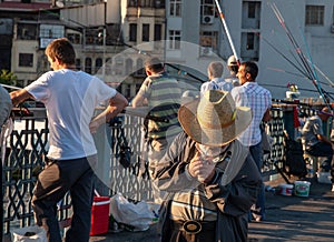 Istanbul / Turkey  old man wearing straw hat lights a cigarette on Galata bridge. Multiple fishermen in the background