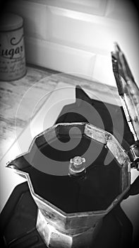 Italian aluminum small opened coffee pot full of black coffee on a kitchen stove top. Black and white