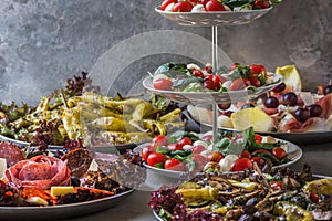 Italian appetizer buffet with grilled vegetables, grilled pepperoni, ham, salami, salad caprese on gray background