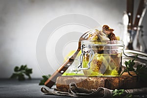 Italian appetizer canned Artichokes in olive oil in glass jar with lemon and herbs on gray kitchen table background, copy space,