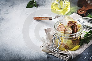Italian appetizer canned Artichokes in olive oil in glass jar with lemon and herbs on gray kitchen table background, copy space,