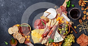 Italian appetizers or antipasto set with gourmet food on black table top view. Delicatessen of cheese and meat snacks with wine