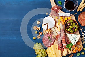 Italian appetizers or antipasto set with gourmet food on blue kitchen table top view. Mixed delicatessen of cheese and meat snacks