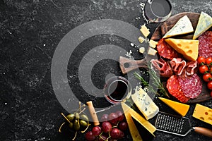 Italian appetizers. Cheese, wine, salami and prosciutto on a black stone background. Top view.