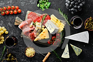 Italian appetizers. Cheese, wine, salami and prosciutto on a black stone background. Top view.