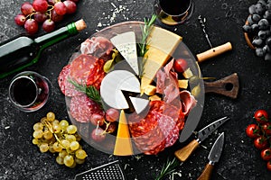 Italian appetizers. Cheese, wine, salami and prosciutto on a black stone background. Top view.