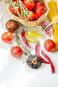 Italian arrabiata pasta ingredients for cooking. Spaghetti tomatoes hot chili peppers culinary herbs olive oil on white table