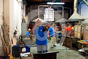 Venice, italy - 20 january 2020: italian artisan glassworker blowing hot glass with traditional, blowpipe in an italian glass