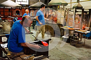 Venice, italy - 20 january 2020: italian artisan glassworker melting hot glass with traditional, blowpipe in an italian glass